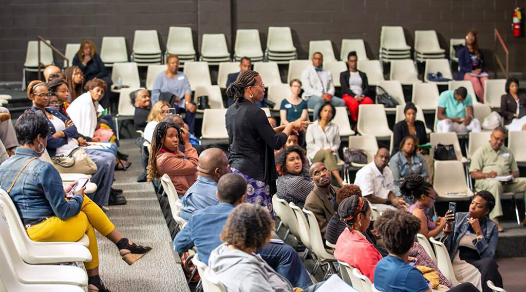 A speaker holding a microphone stands in the middle of a seated crowd in a lecture|A man stands at a podium