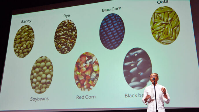 A chef gives a stage presentation about beans and grains|A display of garlic and root vegetables on a table|Four people on stage in front of a projection screen|Members of Team Leverage hugging and smiling|A group of judges seated at a table while one speaks into a microphone|Crowded auditorium at the Museum of Contemporary Art|