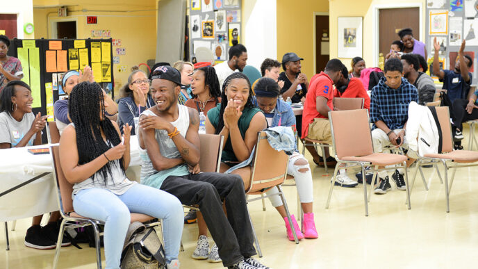 A large group of teenaged sitting in chairs in a basement room