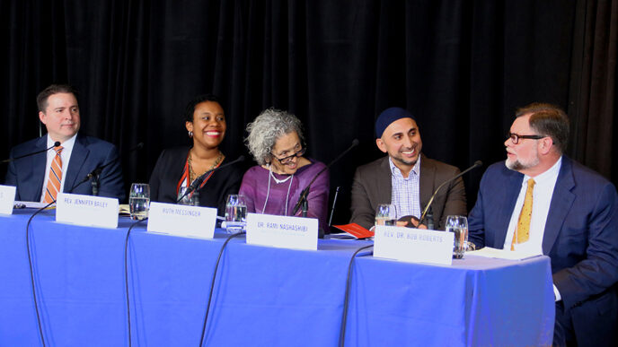 Five people seated behind a table for a panel discussion. The man seated at far right is speaking
