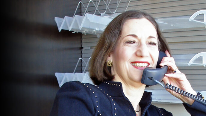 A woman smiles while talking on the phone in an office|A woman smiles while talking on the phone in a wood-paneled office|Three women stand on stage smiling and holding an award plaque