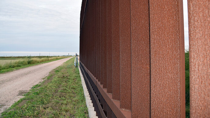 A road runs beside the metal posts of the border fence between Donna