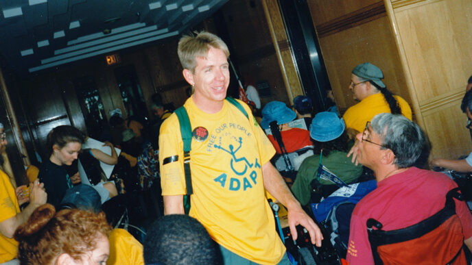 A man wearing a t-shirt that says ADAPT amid a group of people using wheelchairs|Vintage photo of protestors shouting and holding signs.