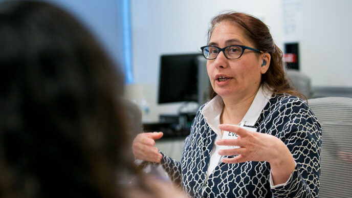 A seated woman gestures with her hands while talking to another person