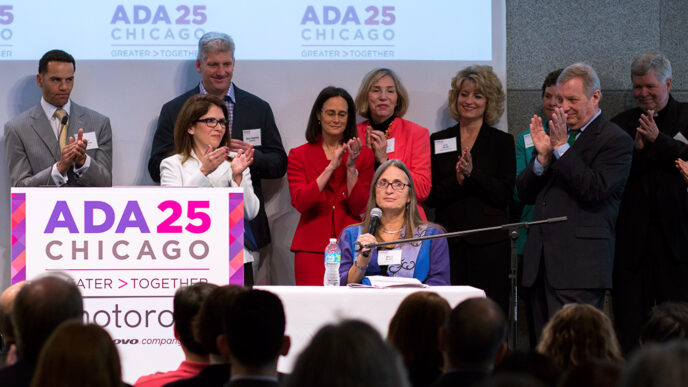 A group of people gathered behind a podium with a sign reading ADA 25 Chicago as one women speaks into a microphone|A group of people gathered behind a podium with a sign reading ADA 25 Chicago as one women speaks into a microphone