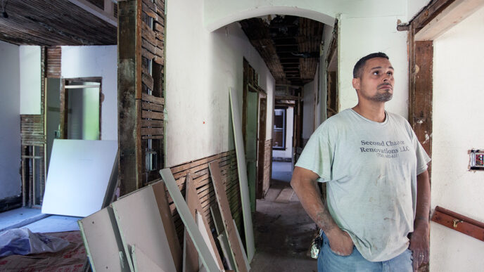 David Figueroa stands inside a vintage building under renovation|Figueroa supervises a crew of construction workers restoring a building foundation
