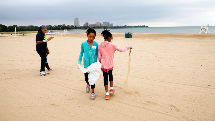 Two sisters pick up trash from the 63rd Street Beach during a cleanup event organized by the Honeycomb Project|A girl and her parents pick up trash at the 63rd Street Beach during a cleanup event organized by the Honeycomb Project|A family checks in to begin beach cleanup|Volunteers collect trash from the sand|A young child watches as girls test the water quality at a 63rd Street Beach cleanup event