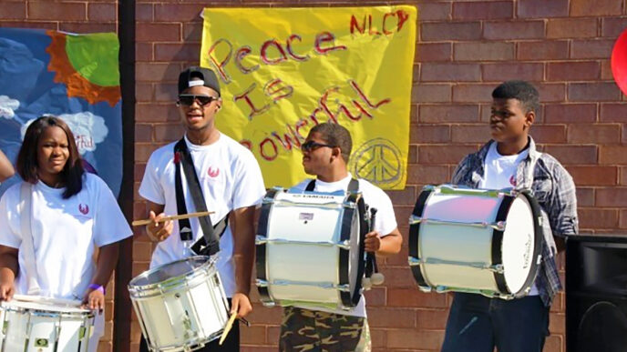 NLCP students stand with marching drums in front of a poster reading 'Peace is Powerful'