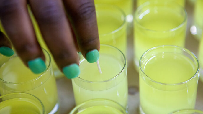 Trainees at Bright Endeavors place wicks into soy votive candles|A training session at the Bright Endeavors workspace|Measuring wax and additives
