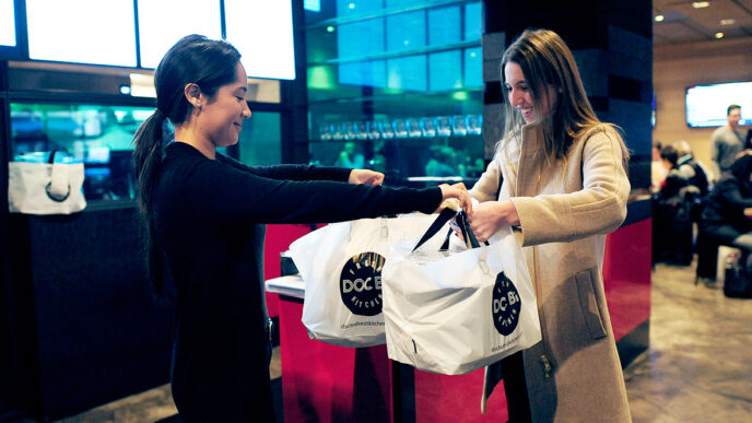 Culinary Care founder Courtney White picks up meals ready to deliver from Doc B's restaurant|Courtney White sits on the hospital bed and talks with a patient during a meal delivery