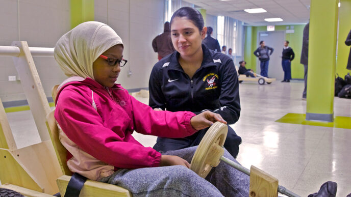 A student from Phoenix Academy helps a young girl steer a wooden boxcar