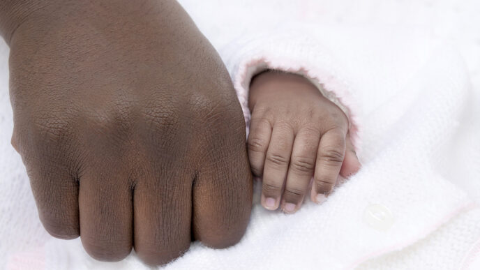 A man's hand rests besides that of a baby