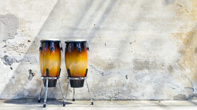 Two conga drums in front of an exterior wall|Carlos Cornier plays drums outside a storefront