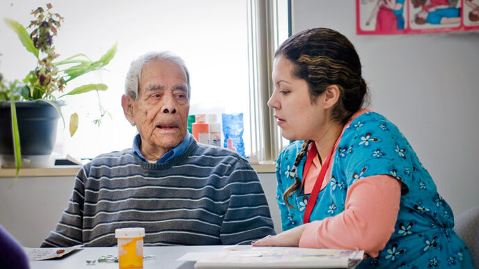 A senior man sits and talks with a health care worker at Casa Central|Map of Illinois color-coded to show the decline in state funding dollars to human services by county