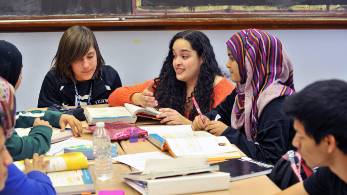 A teacher kneels beside a table of high school students