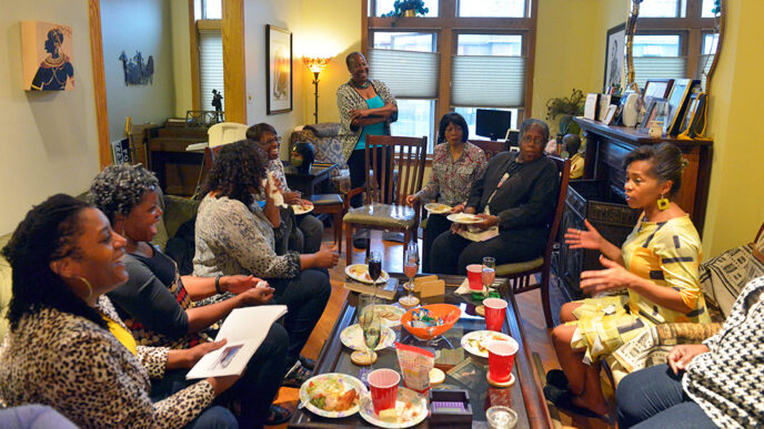 A group of women sit in a living room holding books and having a conversation|A team of people creates a large mosaic on an exterior wall