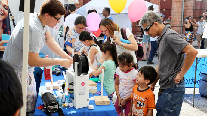 Families examine robotics components at an outdoor festival table