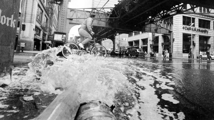 Cyclists pedal along a flooded street in the Loop as water gushes from pipes|