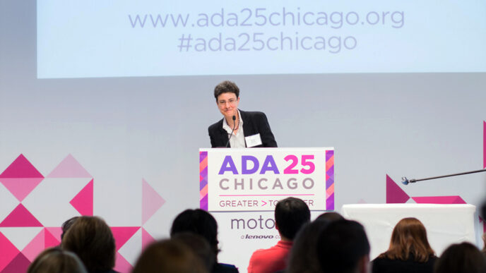 Emily Harris standing on stage at a podium with a sign that reads ADA 25 Chicago - Greater Together|