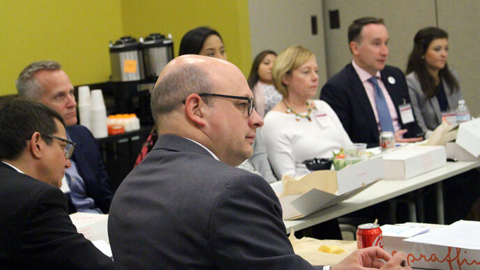 A group of men and women sit around a large table with boxed lunches