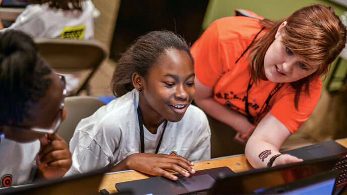 A smiling teenage girl works at a laptop