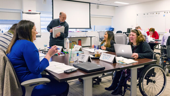 Four people seated in chars and wheelchairs around a table in a conference room