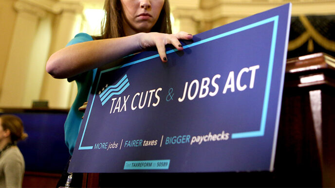 A young staffer affixes a sign reading Tax Cuts and Jobs Act to a podium