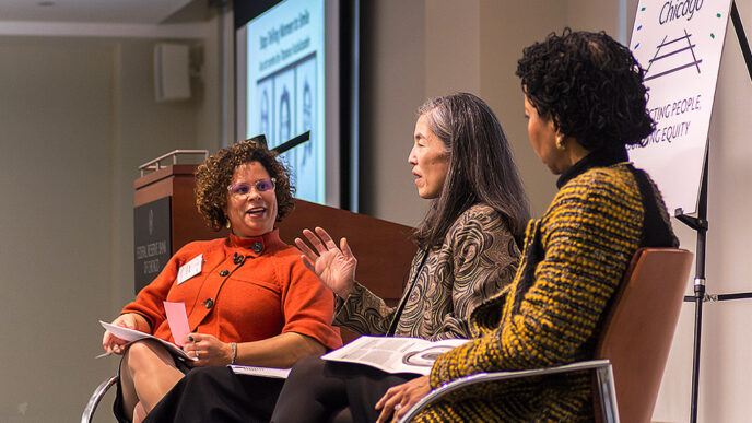 Three women sit in chairs in a stage