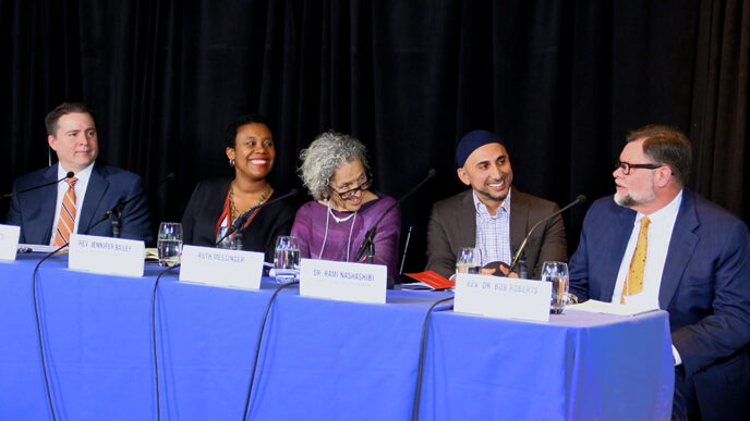 Five people seated behind a table for a panel discussion. The man seated at far right is speaking