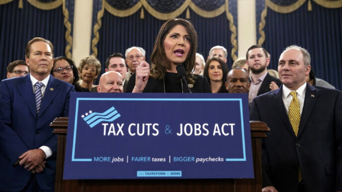 Rep. Kristi Noem of South Dakota stands at a podium holding a sign reading Tax Cuts and Jobs Act