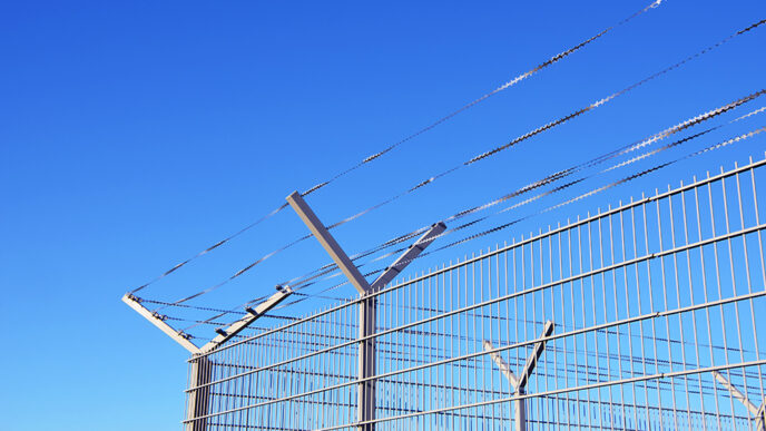 A prison yard fence against a blue sky