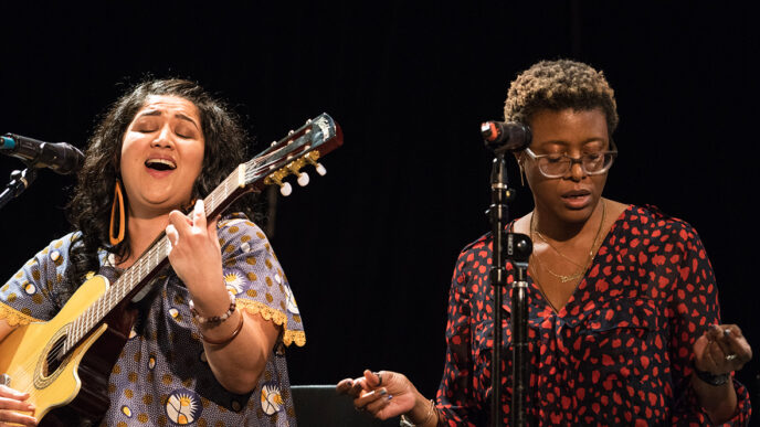 Two women sit on stage in front of microphones