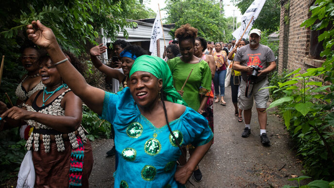 A procession of people march through a residential alley