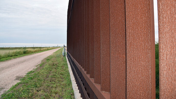 A road runs beside the metal posts of the border fence between Donna