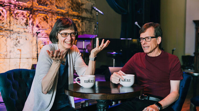Two people sitting and talking at a table in front of a small stage