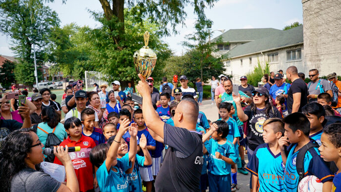 A man in a soccer jersey holds a trophy overhead