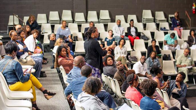 A speaker holding a microphone stands in the middle of a seated crowd in a lecture|A man stands at a podium