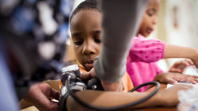 A young boy watches the hands of a nurse fastening a blood pressure cuff around his arm