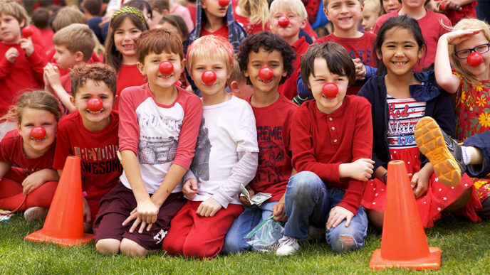 Rows of children sit on the sidelines of a grass playing field