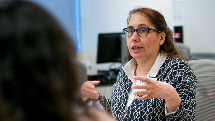 A seated woman gestures with her hands while talking to another person