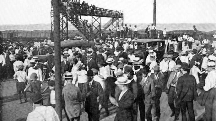Black-and-white archival photo showing a large crowd of men standing at a road crossing
