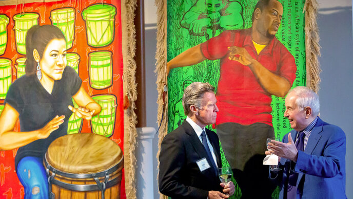 Two men stand together talking in front of large