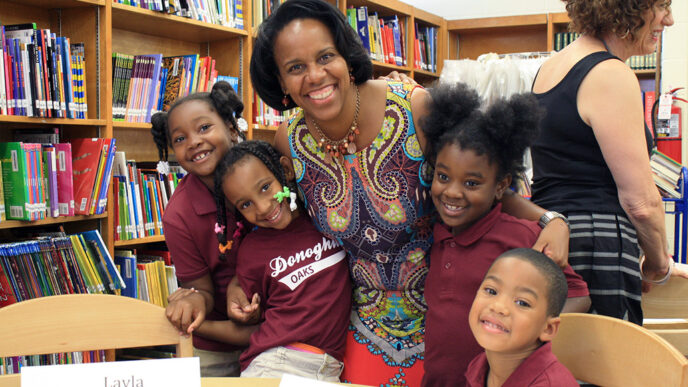A woman and a group of kids smile together at a table in a school library|Head shot of Liz Thompson