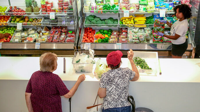 A worker at a food pantry helps two women select produce|Four young girls wearing old-fashioned aviation helmets hold a flag and smile