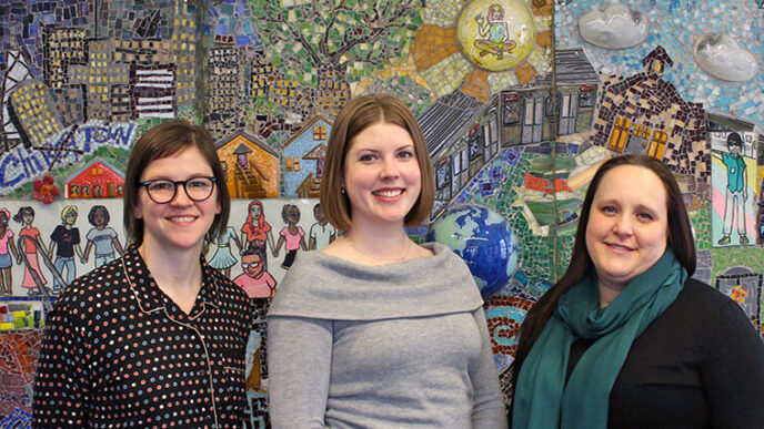 Three people stand in front of a brightly colored mosaic||Three people stand in front of a brightly colored mosaic