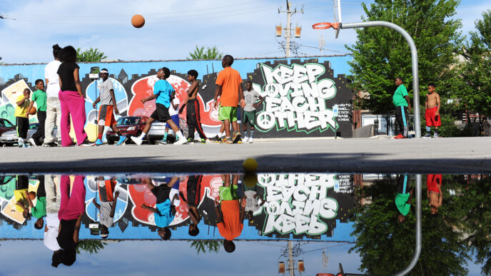 A group plays basketball in front of a mural reading Keep Loving Each Other