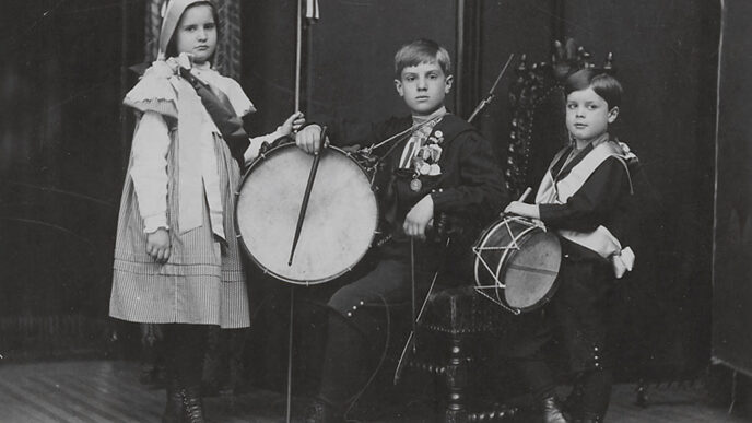 Old black-and-white photo of three children holding drums and American flags